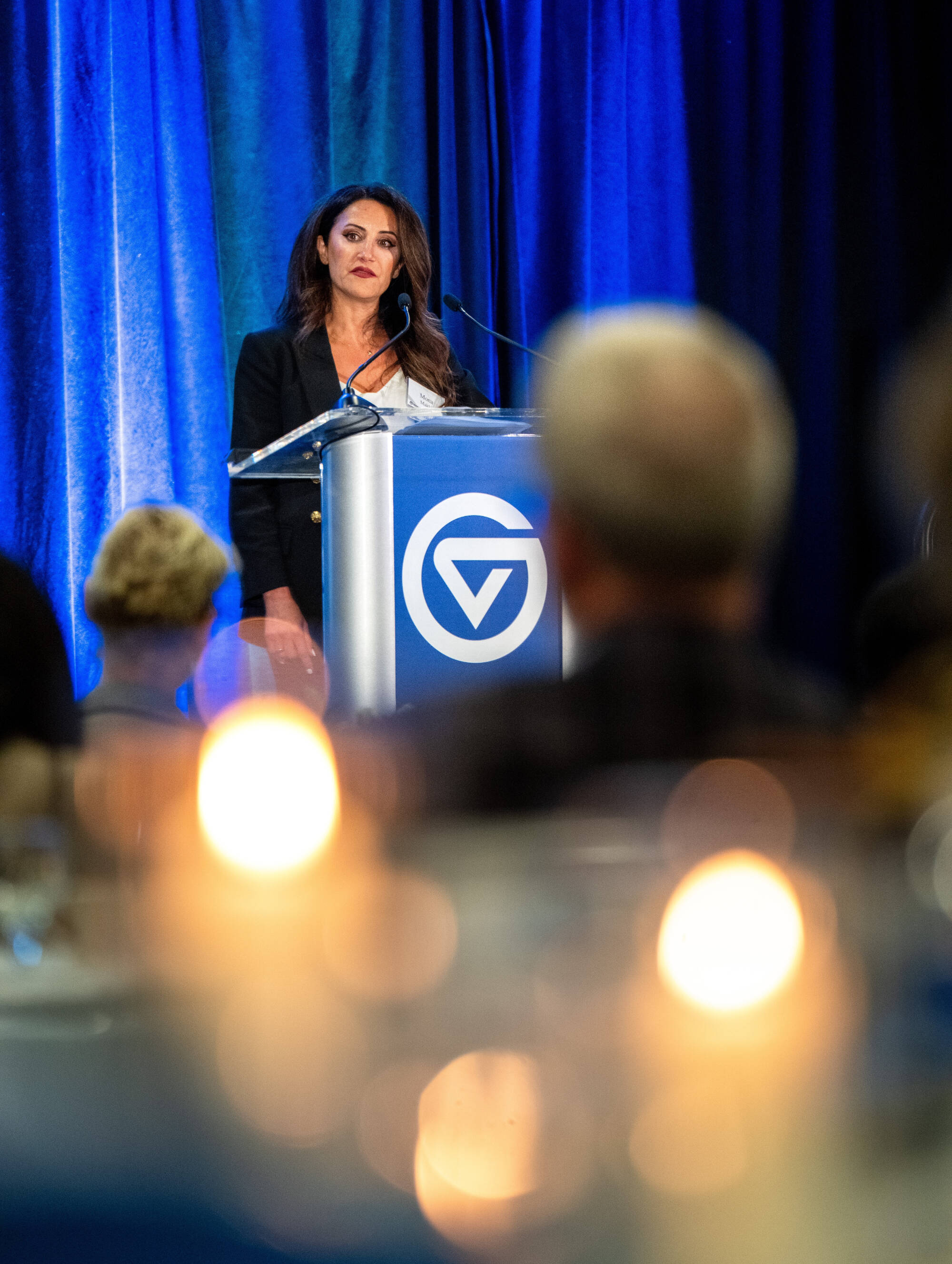 A woman at a podium with candles in the foreground.